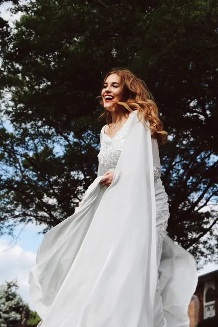 A laughing woman in a flowing white dress under trees