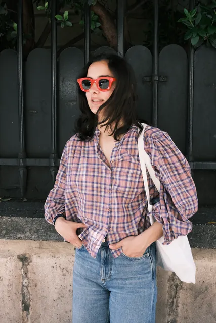 A woman in red sunglasses and a plaid shirt by an iron gate