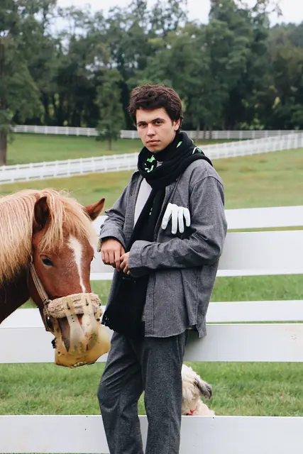 A man in a scarf leaning on a white fence beside a horse