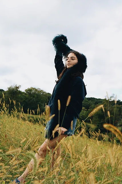 A woman in a black coat reaching up in a field of tall grass