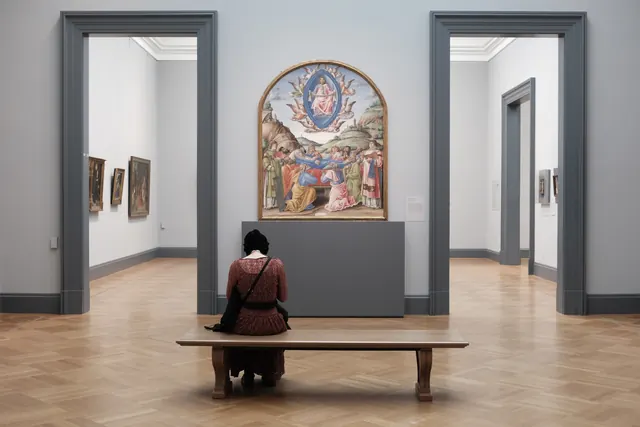 A woman on a bench facing a Renaissance altarpiece in a museum gallery